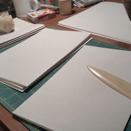 My work table with a stack of folded sheets of paper and a bone folder.