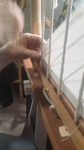 A stack of signatures being sewn to cords on a frame.